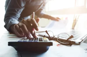 Accountants near me | Person typing on calculator and writing financial documents.