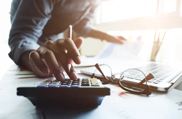 Accountants near me | Person typing on calculator and writing financial documents.
