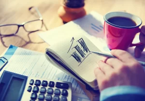 Long-term business goals | Person pointing at paper with bar graph on it, with calculator and mug of coffee.