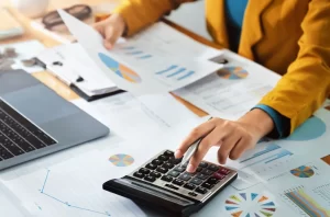 Virtual finance director | Person using calculator on a table with financial documents.
