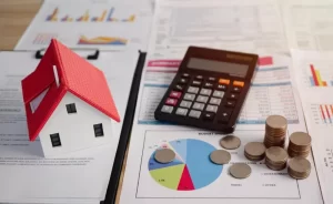 FiMBO | Model house and calculator with money on top of print-outs of financial graphs.