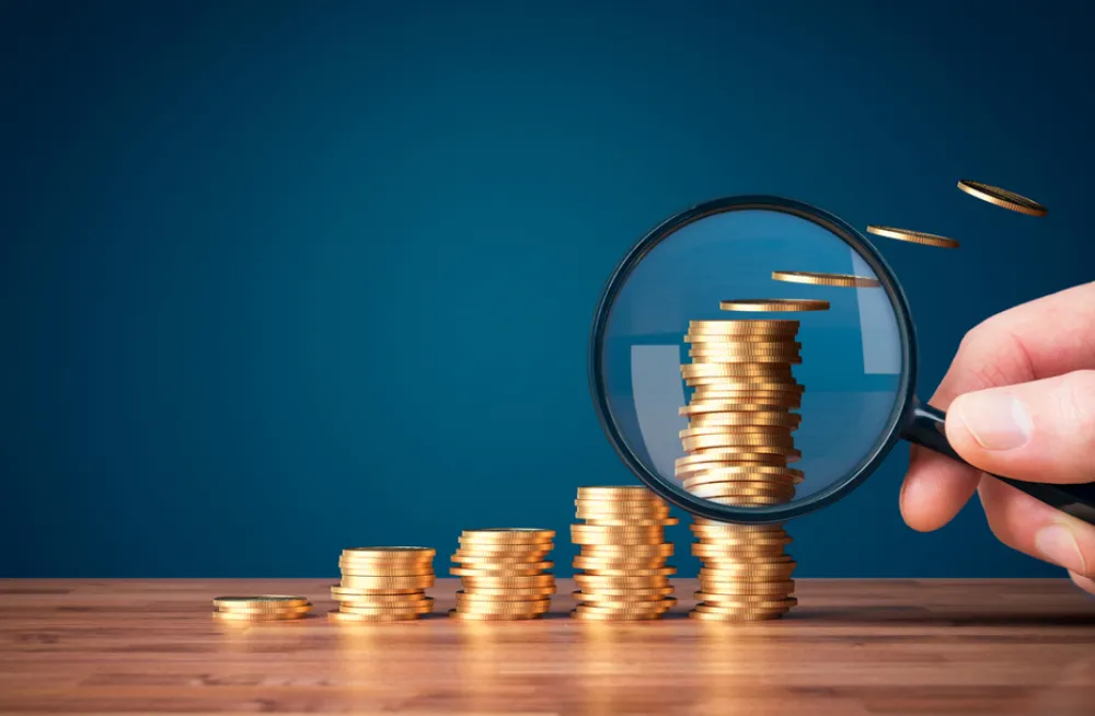 Cash flow forecast | Magnifying glass looking at stacks of coins.